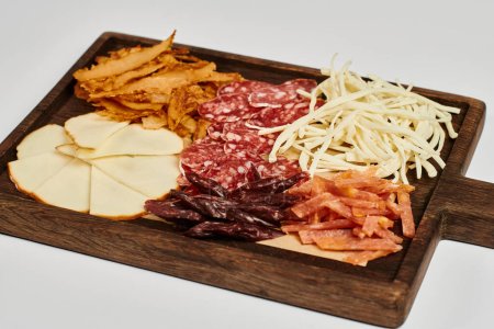 Foto de Tabla de embutidos con sabrosa bandeja de queso, carne seca y rebanadas de salami sobre fondo gris - Imagen libre de derechos