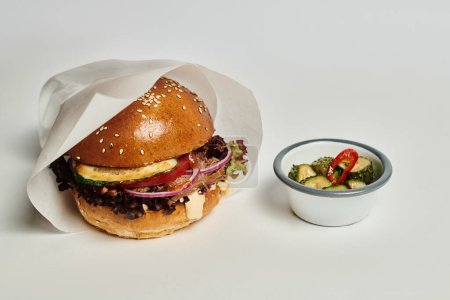 Téléchargez les photos : Délicieux hamburger avec pain de sésame, bœuf et cornichons comme plat d'accompagnement sur plateau en bois sur fond gris - en image libre de droit