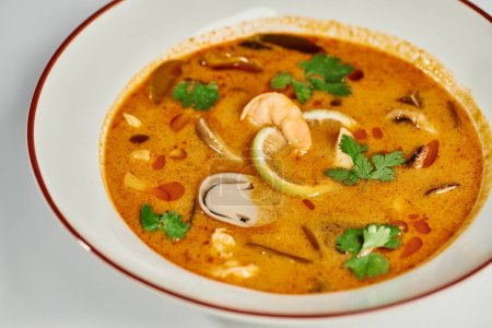 spicy Thai soup with coconut milk, shrimp, lemongrass and cilantro on grey backdrop, Tom yum