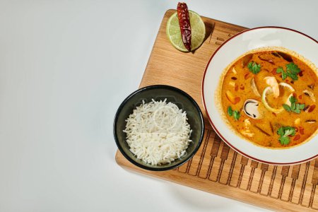Téléchargez les photos : Soupe Tom yum au lait de coco, crevettes, citronnelle et coriandre près d'un bol de riz sur fond gris - en image libre de droit