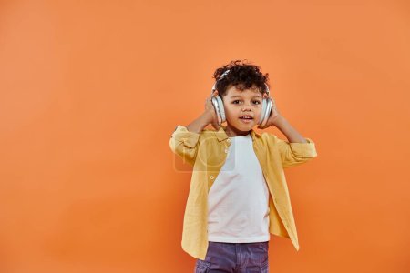 happy and curly african american boy listening music in wireless headphones on orange background
