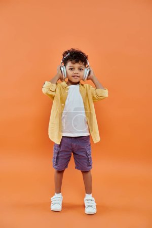 cheerful and curly african american boy listening music in wireless headphones on orange background