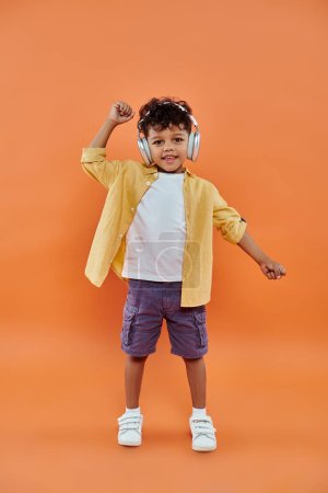 smiling and curly african american boy listening music in wireless headphones on orange background