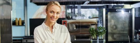 joyful blonde businesswoman smiling at camera in modern cafe, small business, horizontal banner