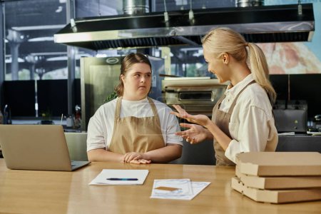 glücklicher Café-Manager erklärt junge Frau mit Down-Syndrom in der Nähe von Laptop und Pizzakartons ihre Pflichten