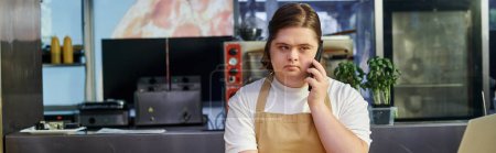 Foto de Mujer joven con síndrome de Down hablando por teléfono móvil mientras trabaja en la cafetería moderna, pancarta - Imagen libre de derechos