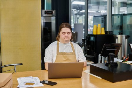 Konzentrierte junge Frau mit Down-Syndrom arbeitet in zeitgenössischem Café am Laptop am Tresen
