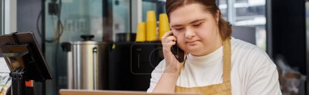 mujer joven con discapacidad mental hablando en el teléfono inteligente mientras trabaja en la cafetería moderna, pancarta