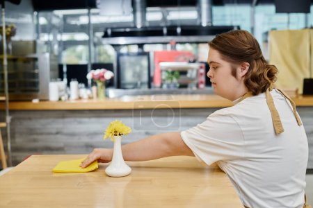 mujer joven con trastorno mental limpiando mesa con trapo mientras trabaja en la cafetería moderna, inclusividad