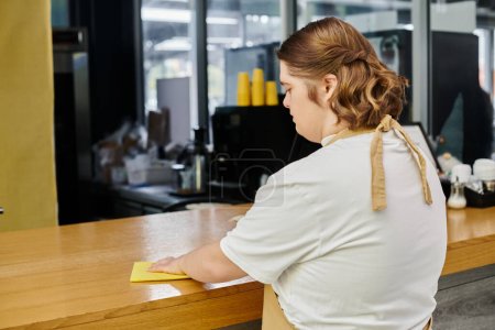 joven empleada con síndrome de Down que trabaja en la cafetería moderna y contador de limpieza con trapo