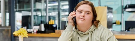 mujer joven con discapacidad mental hablando por teléfono móvil en la cafetería moderna y acogedora, pancarta