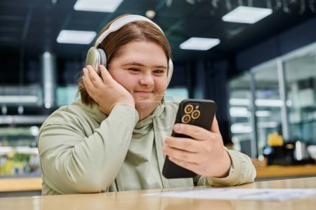 fröhliche Frau mit geistiger Störung hält Smartphone in der Hand und hört Musik über Kopfhörer im Café