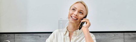 mujer rubia alegre sonriendo durante la conversación en el teléfono móvil en la cafetería, pancarta horizontal