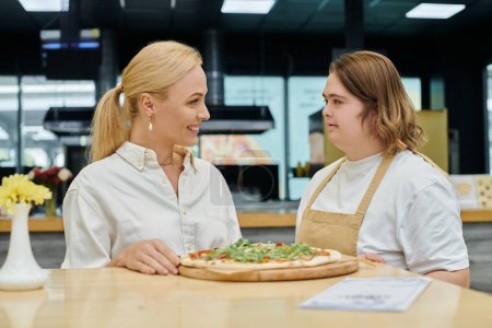 young waitress with mental disorder serving delicious pizza near smiling woman in modern cafe