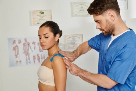 handsome bearded doctor putting kinesio tape on shoulder of his patient on appointment, healthcare