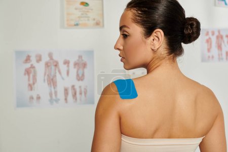 back view of beautiful young woman with kinesio tapes on her shoulder during appointment, healthcare