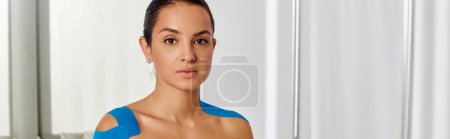 mujer atractiva paciente con cintas kinesiológicas en su cuerpo mirando a la cámara, pancarta