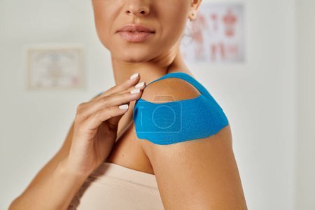 Téléchargez les photos : Jeune patiente avec des bandes kinésiologiques sur l'épaule pendant le rendez-vous, soins de santé - en image libre de droit