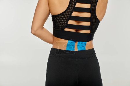vista recortada de una joven en ropa deportiva negra posando con cintas kinesiológicas en la espalda