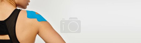 Foto de Vista recortada de la joven mujer en ropa deportiva negro con cintas cinesiológicas en el hombro, pancarta - Imagen libre de derechos