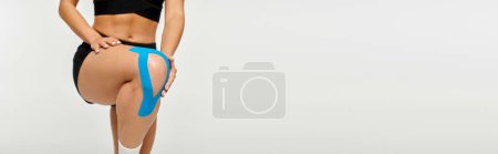 Téléchargez les photos : Vue recadrée de la jeune femme en tenue de sport posant avec des bandes kinésiologiques sur son genou, bannière - en image libre de droit