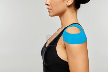 abgeschnittene Ansicht einer jungen Frau in Sportkleidung, die im Profil mit kinesiologischen Bändern auf der Schulter posiert