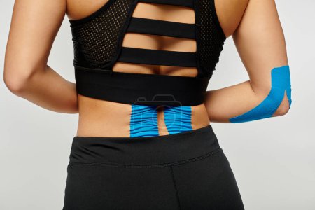 Foto de Vista recortada de mujer joven en ropa deportiva con cintas kinesiológicas en su espalda sobre fondo gris - Imagen libre de derechos