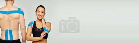 fröhliche Frau und sportlicher Mann mit kinesiologischen Bändern am Körper vor grauem Hintergrund, Banner