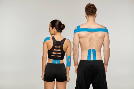 Photo for Back view of attractive woman and man in black sport outfits posing with kinesiological tapes - Royalty Free Image