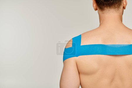Photo for Back view of sporty male model with kinesiological tapes on his shoulder and back on gray backdrop - Royalty Free Image