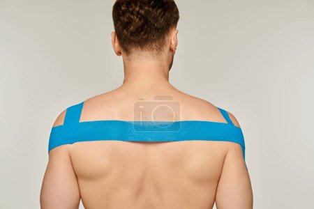 Téléchargez les photos : Vue arrière du modèle masculin athlétique posant avec des bandes kinésiologiques sur ses épaules et son dos - en image libre de droit