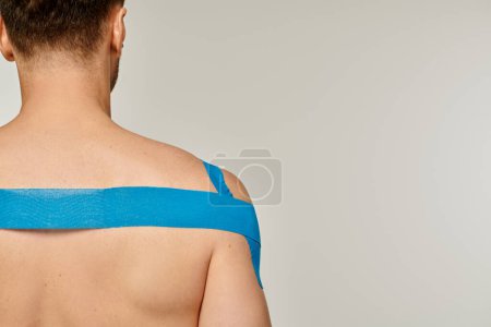 Foto de Vista posterior del hombre deportivo con cintas kinesiológicas en sus hombros y espalda sobre fondo gris - Imagen libre de derechos