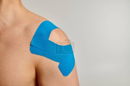 Foto de Vista recortada del hombre con cintas cinesiológicas azules en su hombro posando sobre fondo gris - Imagen libre de derechos