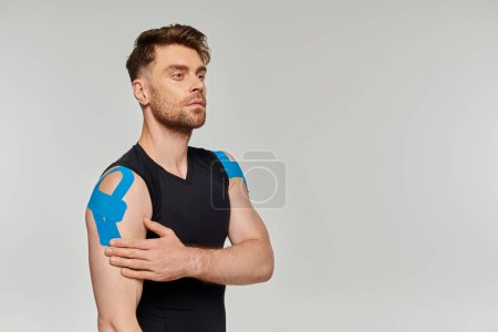 Photo for Good looking bearded man in black sport attire posing with kinesiological tapes and looking away - Royalty Free Image