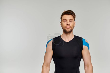 Photo for Handsome bearded man in black sport wear with kinesiological tapes on body looking at camera - Royalty Free Image