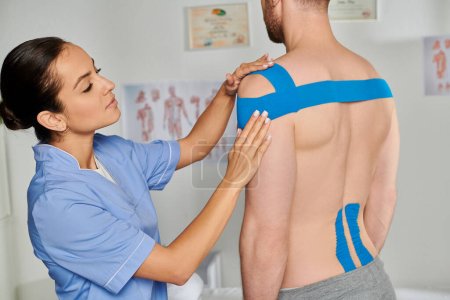 Photo for Attractive young doctor putting kinesiological tapes on her bearded male patient, healthcare - Royalty Free Image