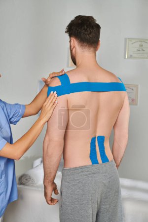 Foto de Vista recortada del joven médico junto a su paciente masculino en pantalones de chándal con cintas cinesiológicas - Imagen libre de derechos