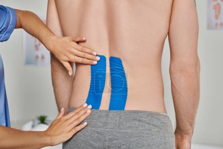 Foto de Vista recortada de las manos de la doctora poniendo cintas de kinesio en la espalda de su paciente masculino, cuidado de la salud - Imagen libre de derechos