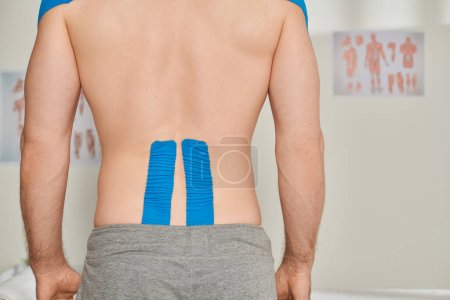 cropped back view of man in gray sweatpants with kinesiological tapes on his back, healthcare