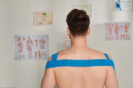 Foto de Vista posterior del hombre con cintas kinesiológicas en sus hombros y espalda durante la cita, atención médica - Imagen libre de derechos