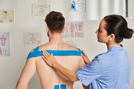 Foto de Hermosa joven doctora poniendo cintas kinesiológicas en la espalda y hombros de su paciente, cuidado de la salud - Imagen libre de derechos