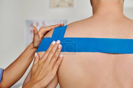 Photo for Cropped view of hand of young female doctor putting kinesio tape on shoulder of her patient - Royalty Free Image