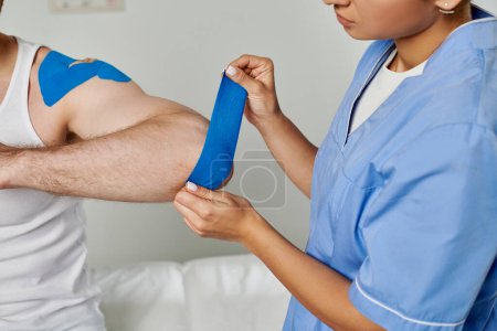 Photo for Cropped view of female doctor in medical costume putting kinesiological tape on elbow of her patient - Royalty Free Image