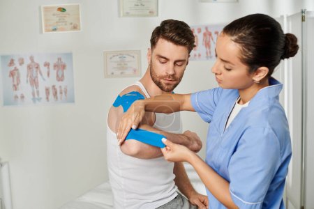 Photo for Good looking man sitting and watching his young doctor putting kinesio tape on his elbow, healthcare - Royalty Free Image