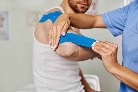 Photo for Cropped view of female doctor putting kinesio tape on elbow of her bearded patient, healthcare - Royalty Free Image