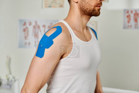 Foto de Vista recortada del hombre barbudo en traje casual con cintas kinesiológicas en el hombro, atención médica - Imagen libre de derechos