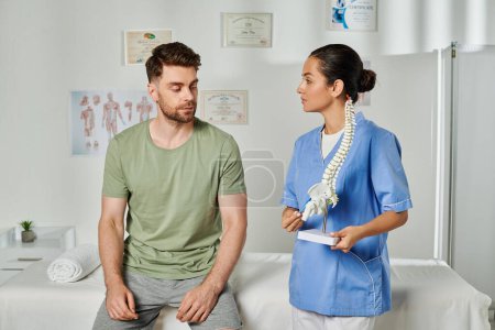 handsome bearded man looking at spine model that his young doctor holding in hands, healthcare