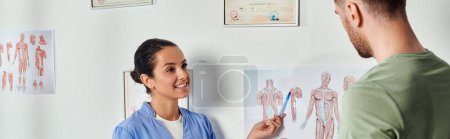 Foto de Médico alegre en traje médico mostrando esquemas de anatomía a su paciente, cuidado de la salud, bandera - Imagen libre de derechos