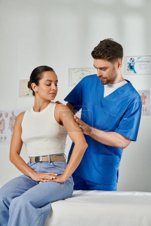 attractive young woman in casual attire watching how doctor checking her shoulder, healthcare