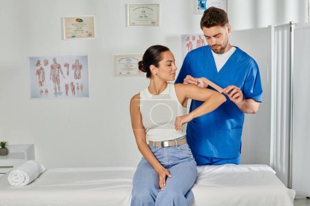 Photo for Attractive young woman in casual attire looking at her doctor putting kinesio tape on her elbow - Royalty Free Image